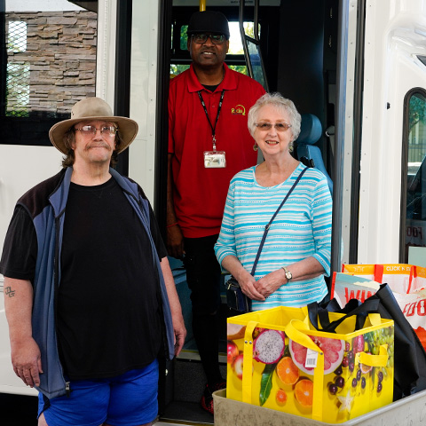 Two older Ride Connection customers and their driver, a black man standing at the door of a shuttle for a grocery trip.