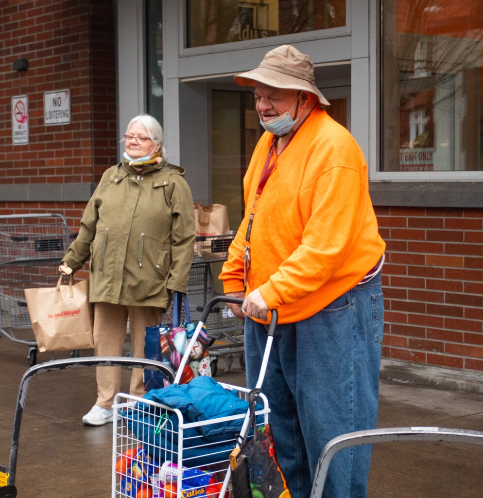 An older white man and woman stand with groceries, waiting to board a Ride Connection shuttle
