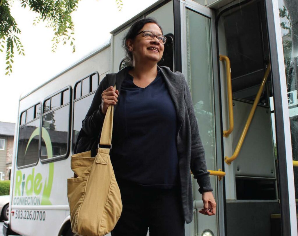 A latina woman exits a Ride Connection shuttle while carrying a bag on her shoulder.