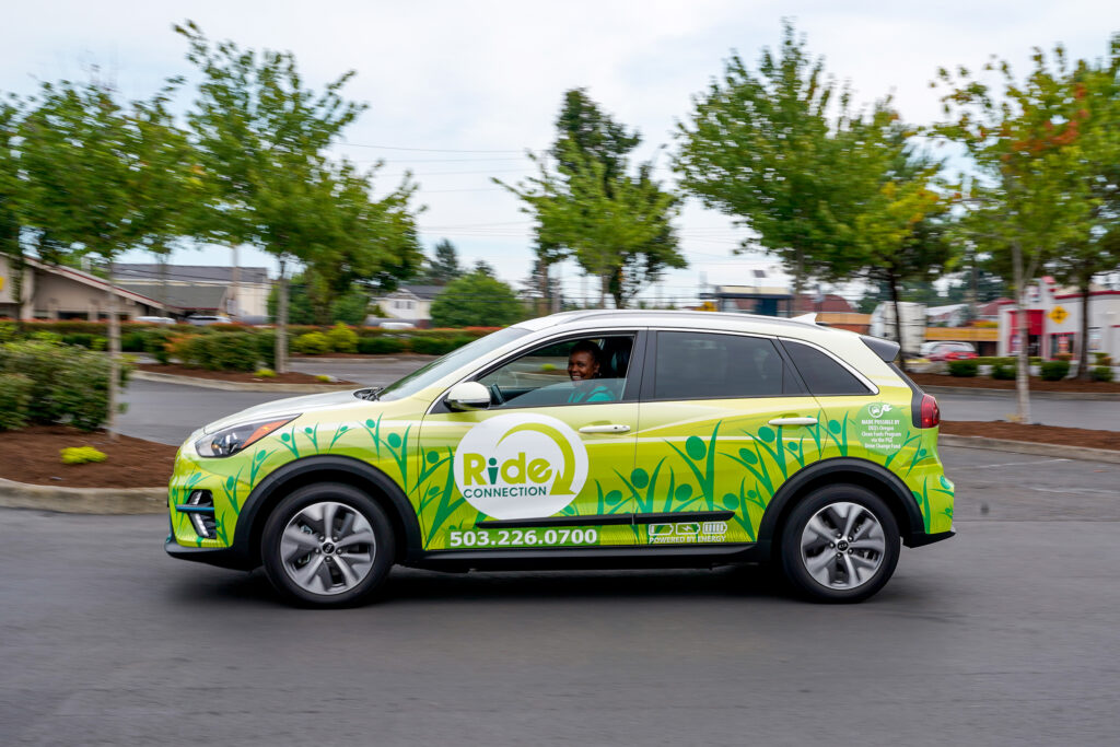 A black female Ride Connection driver drives her electric vehicle through a parking lot