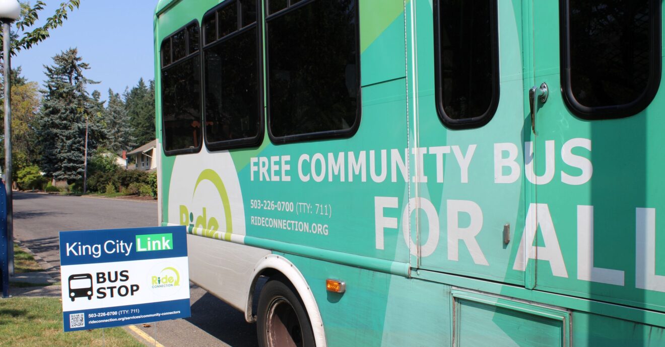 A blue and green King City Link Shuttle parked next to a bus stop yard sign.