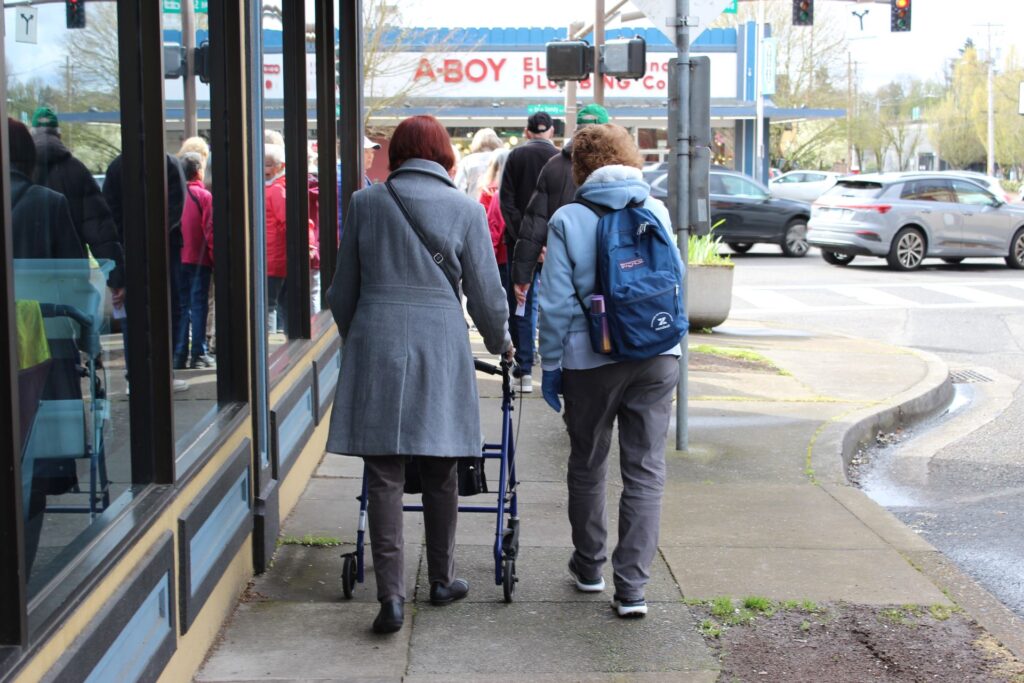 Two people, one with a mobility device, with their backs to the camera are walking with a group on a trip.